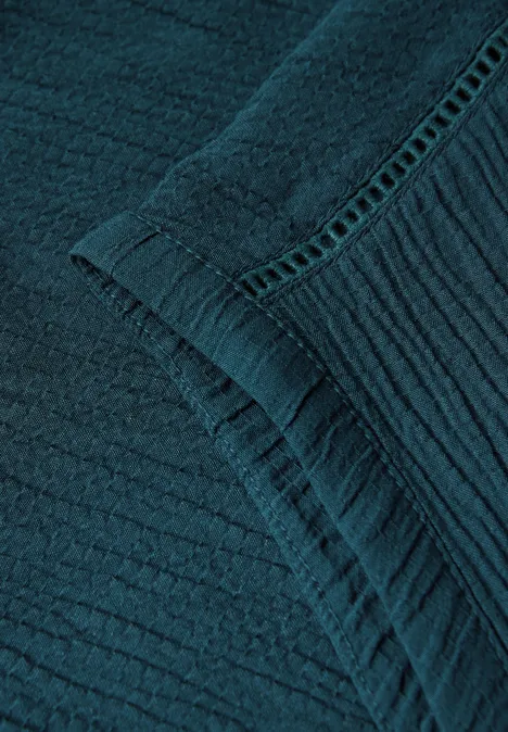 Nahaufnahme von blau-grünem, strukturiertem Stoff mit feinen Nähten.